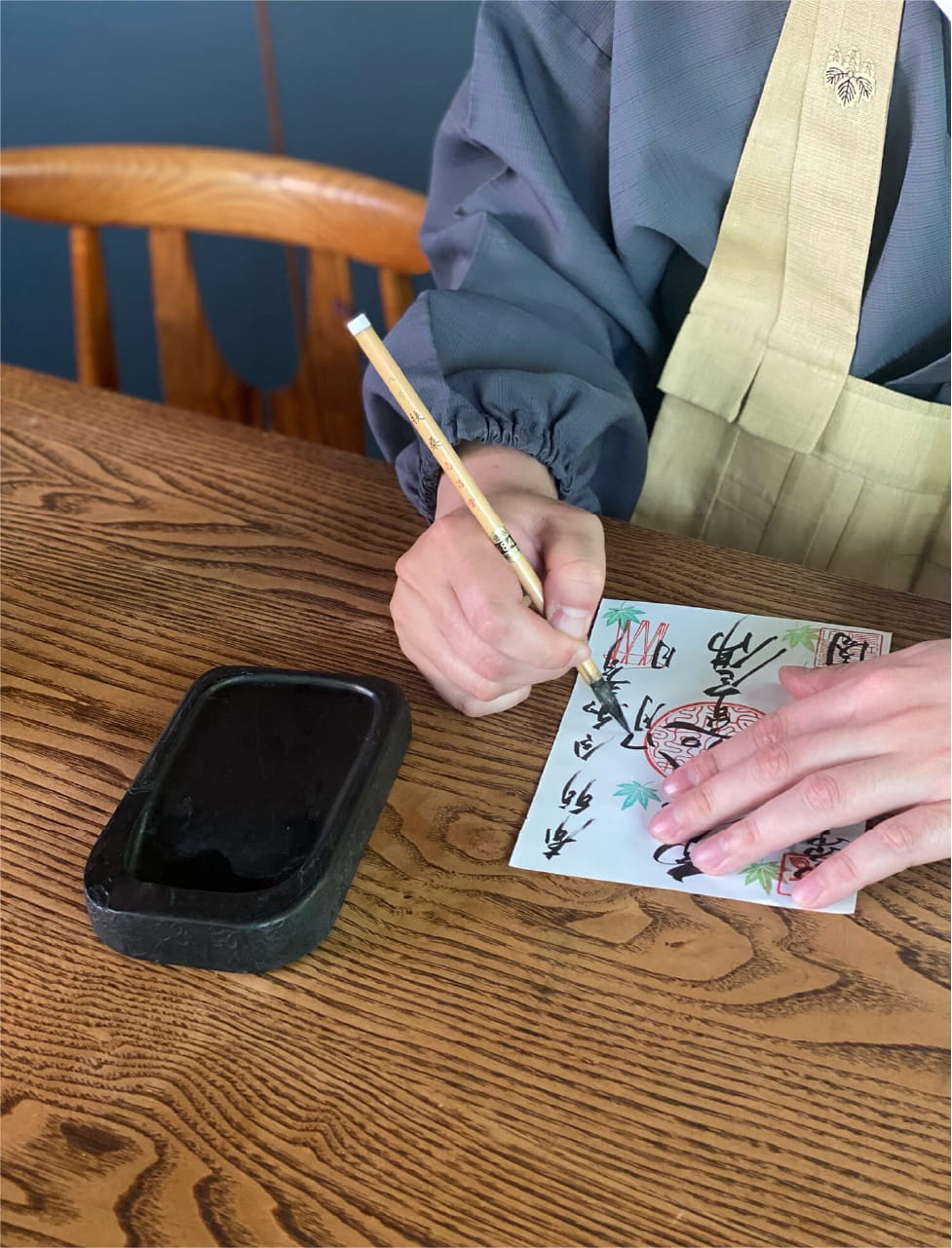 伝統的な衣服を着た人が木製の机で筆と墨を使って文字を書いている様子