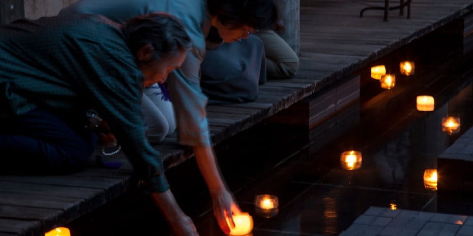 夕暮れ時にキャンドルライトによって照らされた穏やかな水辺で、二人の女性がキャンドルを水に浮かせている様子